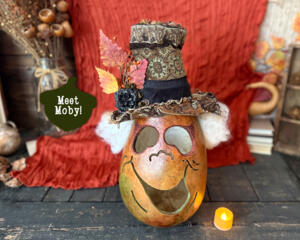 A monster pumpkin character made from a real, dried gourd. The monster is green with a big grin and top hat. He has white ghostly hair.